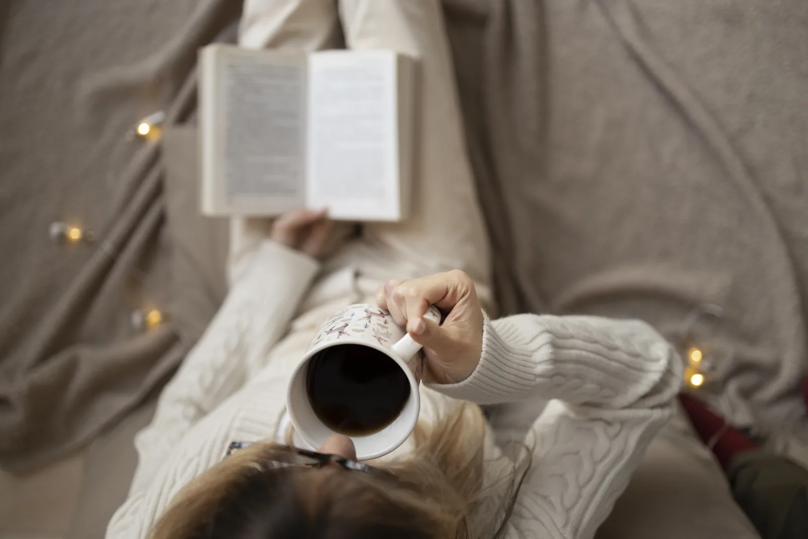 Frau liest entspannt ein gedrucktes Buch mit einer Tasse Kaffee in der Hand
