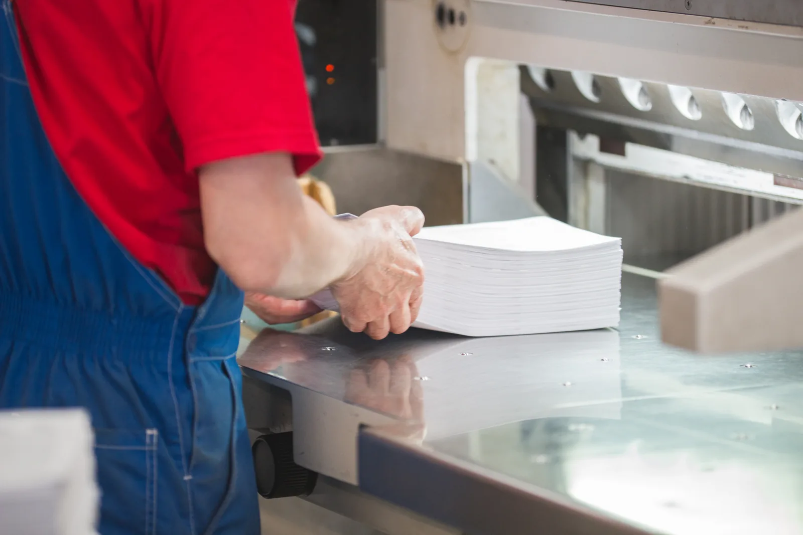 Hände eines Druckerei-Mitarbeiters legen einen Papierstapel in die Schneidemaschine