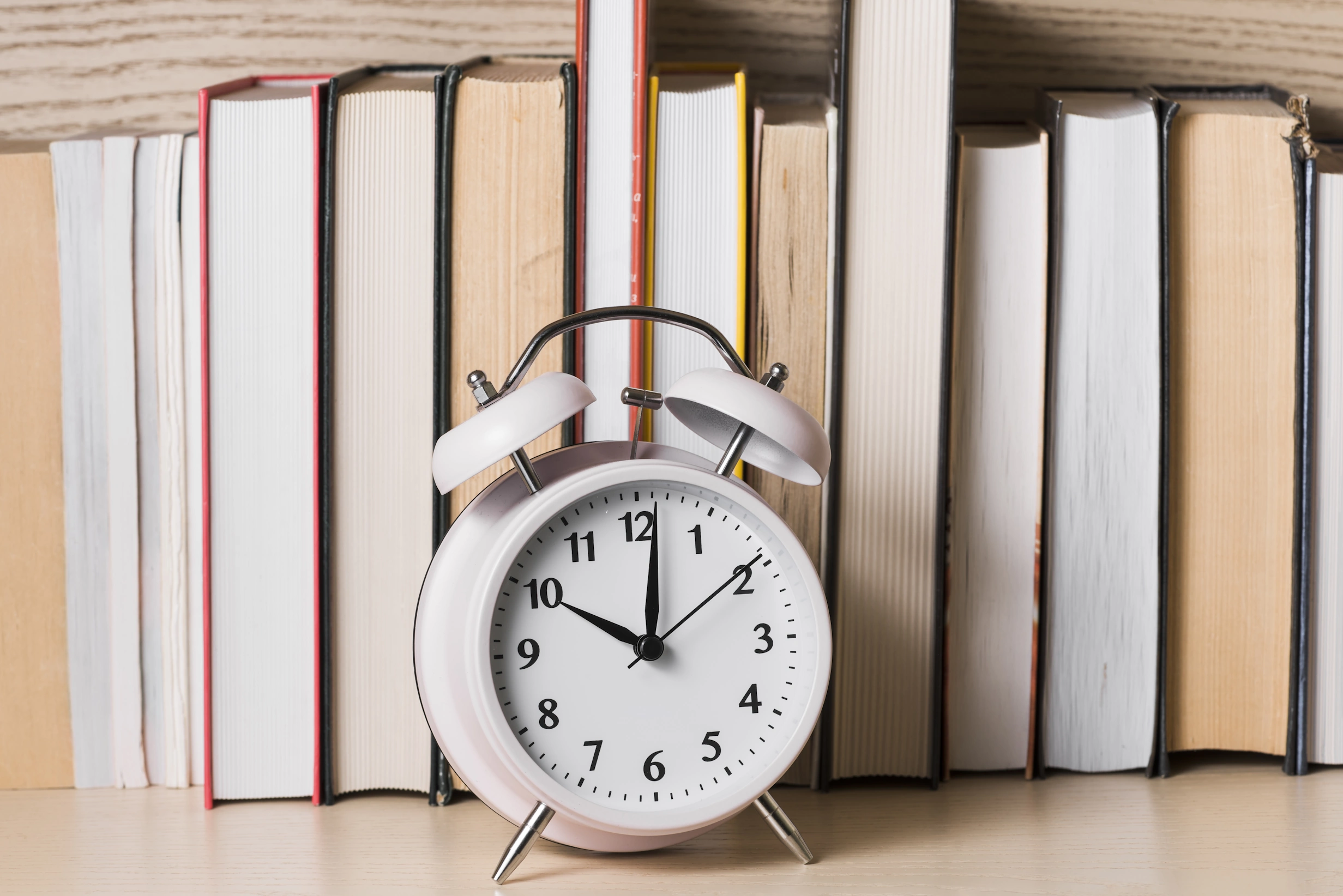 buchlaunch-planen Ein Wecker vor einer Reihe von Büchern.