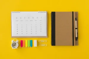 Eine kleine Uhr, ein Kalender, Post-its und ein Planer mit Stift auf gelbem Untergrund.