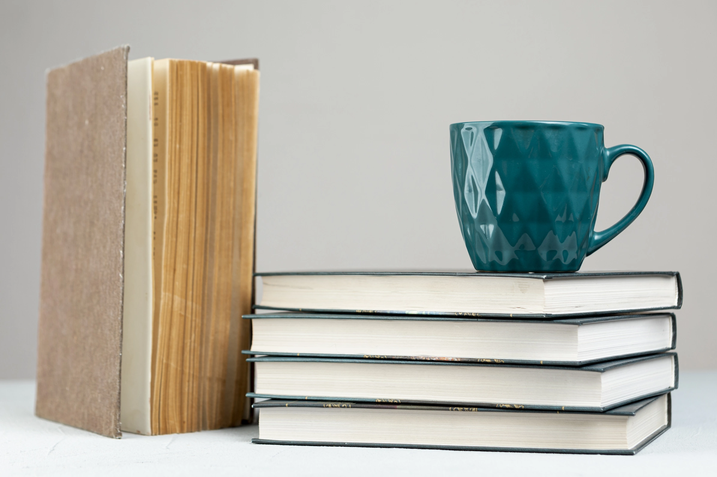 Eine Tasse steht auf einem Bücherstapel. Daneben steht ein altes Buch mit vergilbtem Papier.